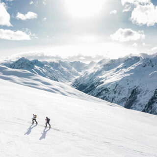 Zwei Personen auf einer Skitour vor verschneitem Bergpanorama.