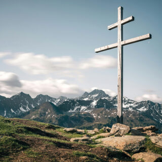 Gipfelkreuz im Vordergrund und Bergpanorama im Hintergrund.
